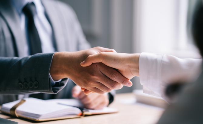 Two people shake hands over a desk