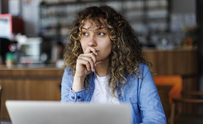 A woman sits at a laptop with a pensive look on her face