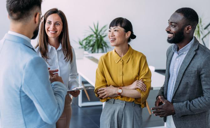 A group of people wearing professional clothing stand together, having a conversation