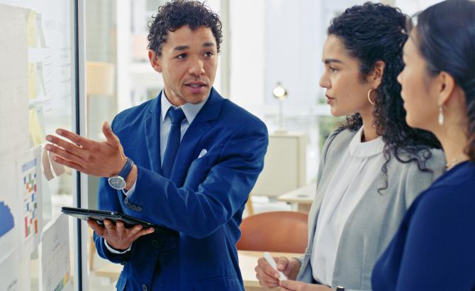 Three people stand and look at a whiteboard covered in papers