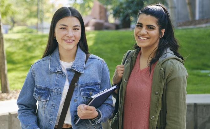 Two students standing on campus, smiling at camera