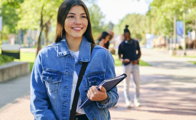 Law student standing on walkway with books in hand, smiling